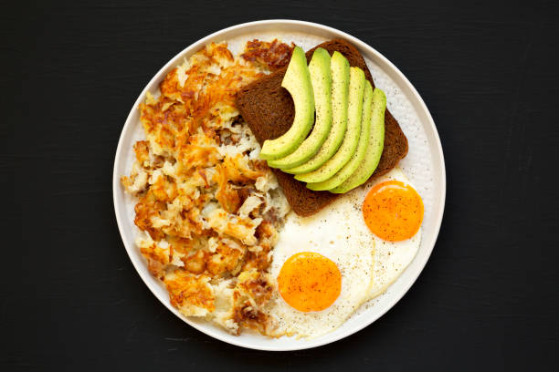 sabrosos hashbrowns fritos caseros y huevos en un plato en una superficie negra, vista superior. lay plana, arriba, desde arriba. - hash brown gold food vegetable fotografías e imágenes de stock