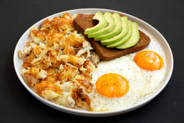 sabrosos hashbrowns fritos caseros y huevos en un plato sobre un fondo negro, vista lateral. - hash brown gold food vegetable fotografías e imágenes de stock