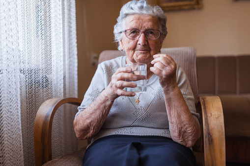 Happy old lady holding glass of water when resting at home