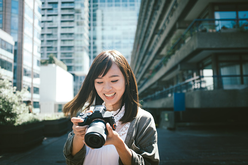 Asian cheerful girl reviewing picture from her camera on the street.