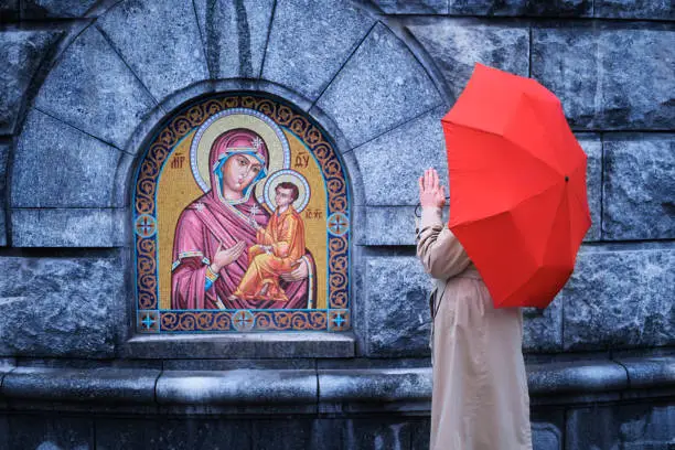 Photo of Praying woman with red umbrella at the Christian icon
