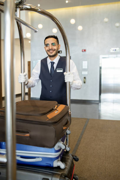 istock Young porter in uniform pushing cart with baggage 1323260470