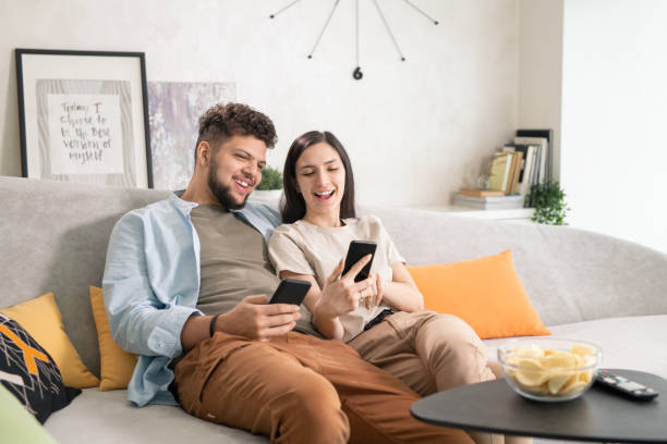 istock Cheerful couple using smartphones while resting on couch 1323260597