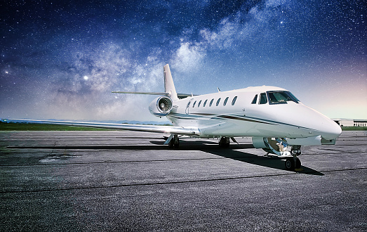 A private white jet airplane sitting on the runway with a mystical starry night sky.