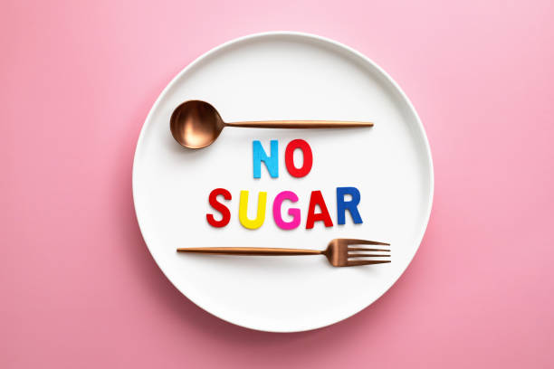 Multi colored "No Sugar" alphabet letter on a plate with spoon and fork against pink background stock photo