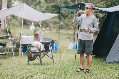 asian chinese senior man brushing teeth outside camping tent after wake up in the morning