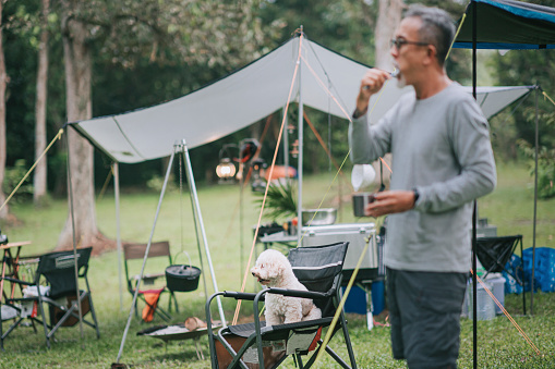 asian chinese senior man brushing teeth outside camping tent after wake up in the morning
