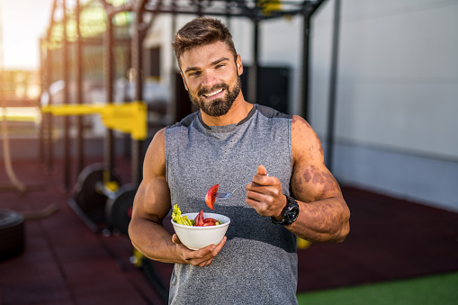 Smiling young male athlete eating a vegetable salad at the gym.