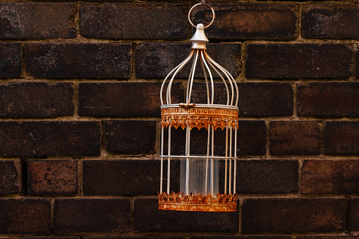 Birdcage-like candle holder hanging on a brick wall.