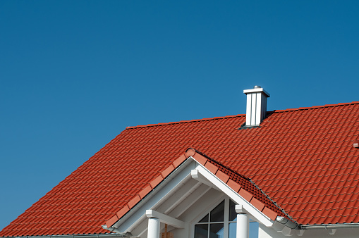 view to a tiled roof with a chimney covered with metal plates on a sunny day with clear blue sky