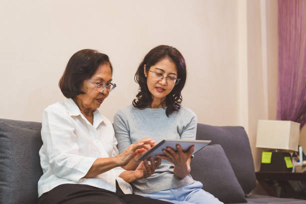 istock Asian daughter and senior mother working with digital tablet computer while sitting on sofa in living room at home 1323286560