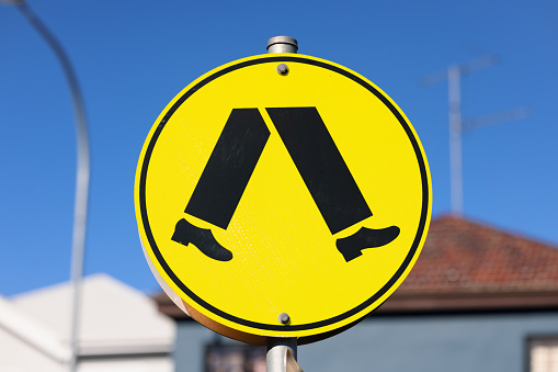 Pedestrian crosswalk road sign against a blue sky.