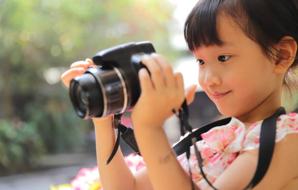 a Asian girl take photos with a digital camera. a smiling Asian girl take photos with a digital camera in a garden. young children pictures stock pictures, royalty-free photos & images