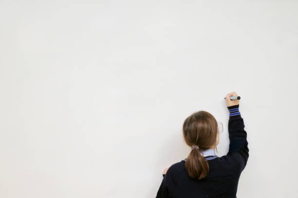 School student writing on a clear whiteboard Rear view of Intermediate high schoolgirl student writing on a clear whiteboard for copy text. kids using smart board stock pictures, royalty-free photos & images