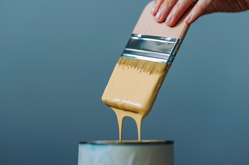 Unrecognizable woman pouring and mixing the light yellow paint in the can with brush