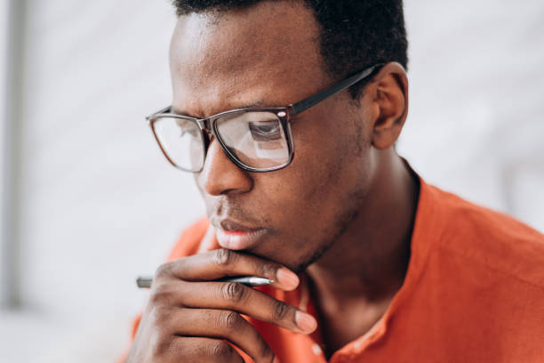 istock Thoughtful black man with glasses and pen in light room 1323307725
