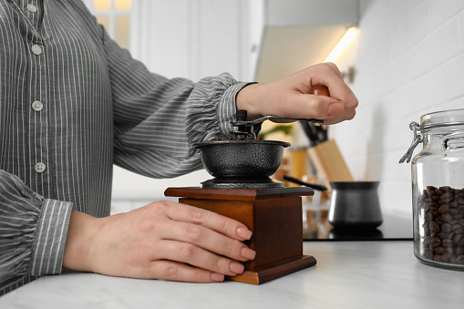 Woman using vintage coffee grinder at countertop indoors, closeup