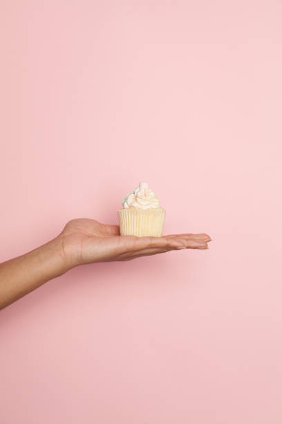 istock Holiday cupcake in female hand on pastel pink background. Minimal background composition 1323310044