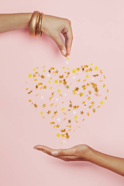 Shiny heart of falling confetti stars and womans hands on pink background Shiny heart of falling confetti stars and womans hands on pink background valentine s day holiday stock pictures, royalty-free photos & images