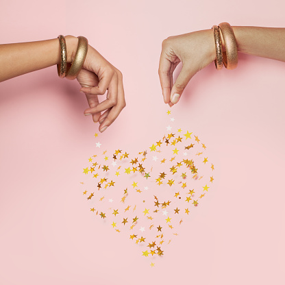 Female hands and falling confetti star. Heart on pink background