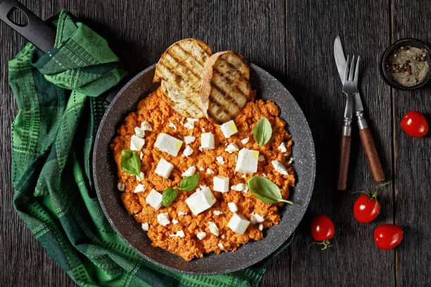 Strapatsada, eggs scrambled with tomatoes and feta cheese in a skillet with toasted bread, horizontal view, greek cuisine, close-up, flat lay