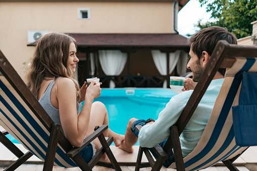 Lovely young couple spend time together at home near the pool while chatting and enjoying tea