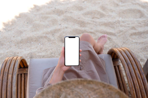 istock a woman holding mobile phone with blank desktop screen while sitting on the beach 1323311201