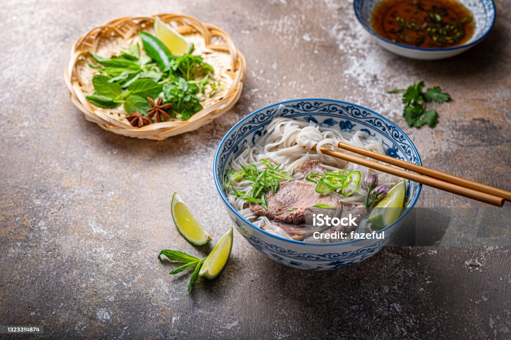 Traditional vietnamese noodle soup pho in bowl, garnished with basil, mint, lime, on concrete background Traditional vietnamese noodle soup pho in bowl, garnished with basil, mint, lime, on concrete background. Ho Chi Minh City Stock Photo