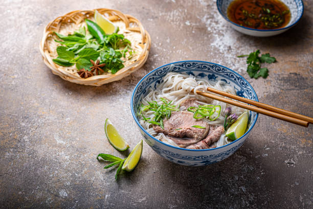 Traditional vietnamese noodle soup pho in bowl, garnished with basil, mint, lime, on concrete background Traditional vietnamese noodle soup pho in bowl, garnished with basil, mint, lime, on concrete background. noodle soup photos stock pictures, royalty-free photos & images