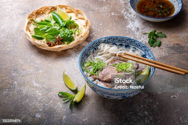 Traditional Vietnamese Noodle Soup Pho In Bowl Garnished With Basil Mint Lime On Concrete Background Stock Photo - Download Image Now