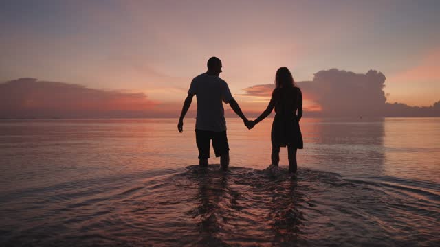 Couple walking into the sea at sunset