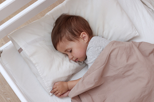 Peaceful adorable toddler baby sleeping on his bed in a room. Sleeping child concept. Two year-old kid sleeps at home.