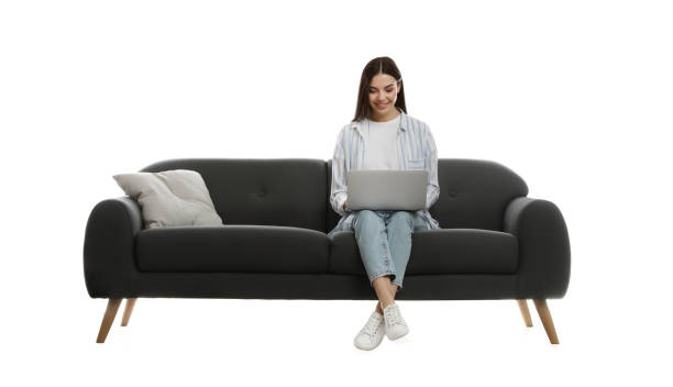 молодая женщина с ноутбуком на удобном сером диване на белом фоне - sofa стоковые фото и изображения