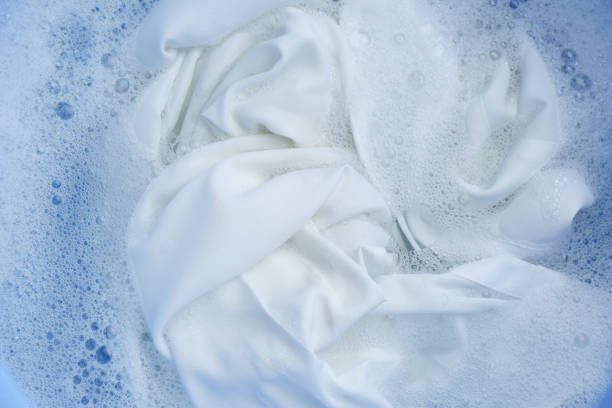 белая одежда в пене, вид сверху. прачечная для мытья рук - washing стоковые фото и изображения