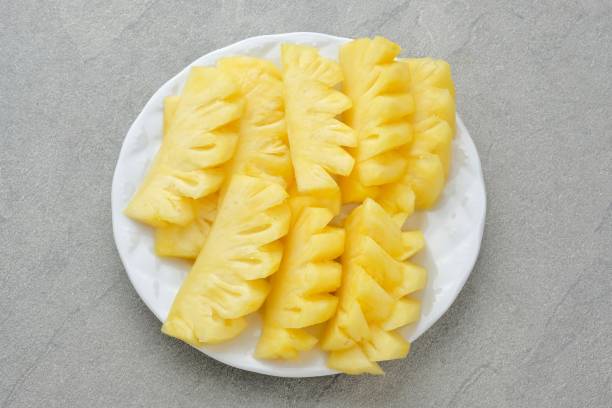 Fresh slices pineapple served in white plate, isolated on a grey background. Close up.