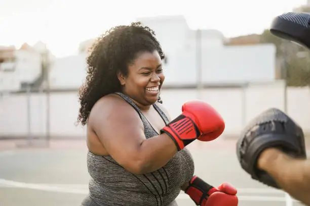 Photo of African curvy woman and personal trainer doing boxing workout session outdoor - Focus on face