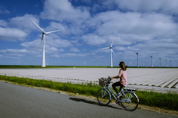 giovane donna bici verde elettrica bicicletta da parco mulino a vento, mulini a vento isolati in una bella giornata luminosa olanda flevoland noordoostpolder - wind turbine fuel and power generation clean industry foto e immagini stock