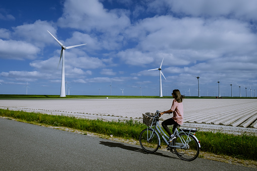 young woman electric green bike bicycle by windmill farm, windmills isolated on a beautiful bright day Netherlands Flevoland Noordoostpolder Holland