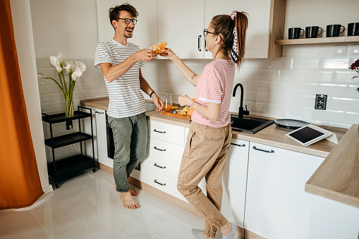 Young couple having morning routine in their apartment, drinking juice in kitchen and talking