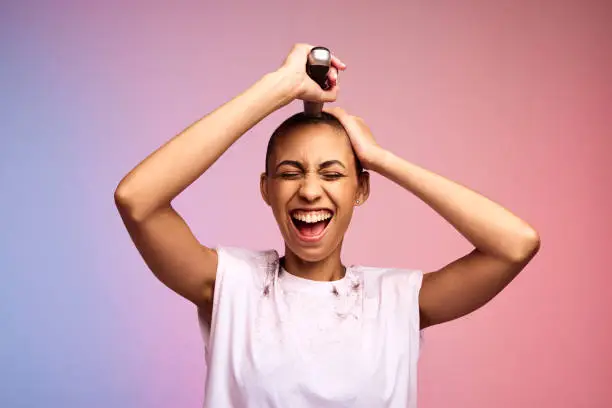 Woman trimming her head to bald on multicolored background. Female shaving off her hair with hair clippers.