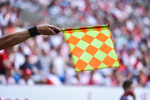 Hand of assistant of football referee with raised flag.