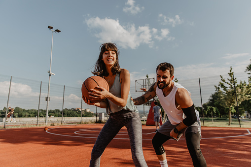 Photo of Cheerful Man and Woman in sports outfit Playing a Basketball Game and Enjoying the Time Together on a Sunny Day.
