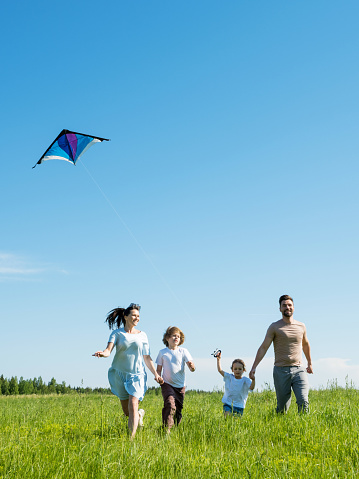 Happy family of mother father children running over a green meadow in summer, fly a kite
