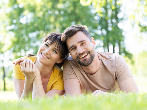 Happy mid adult couple lying outdoors on grass and smiling