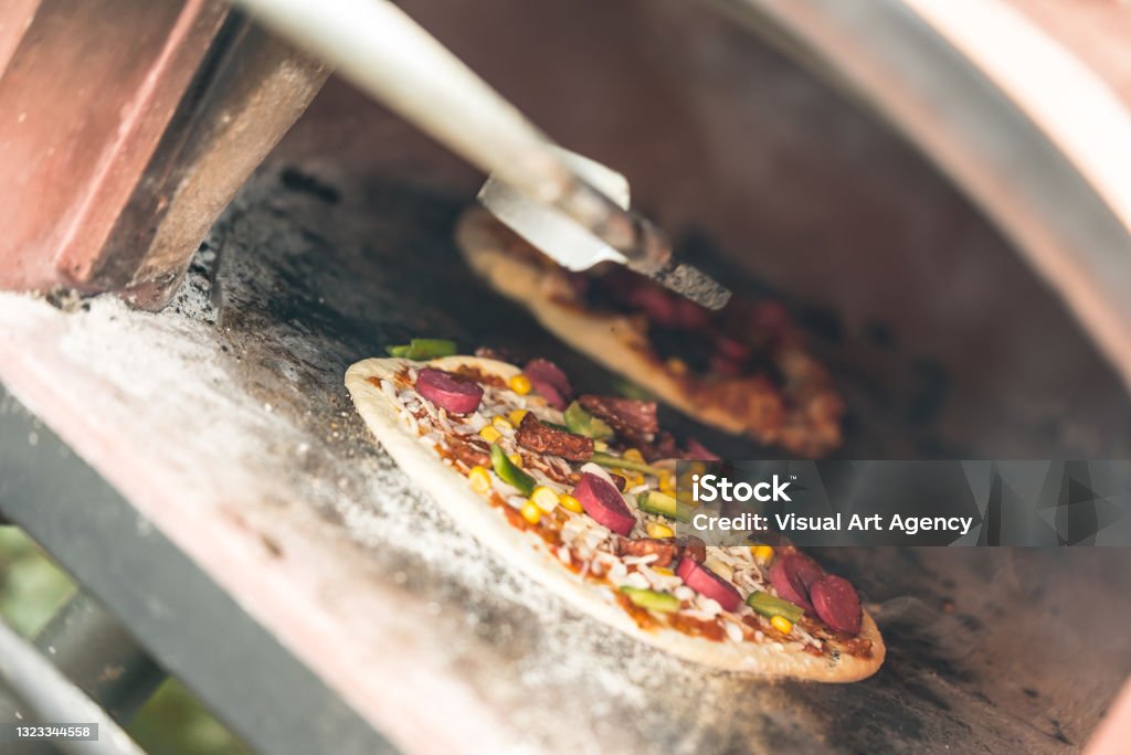 turning the pizza in the stone oven Barbecue - Meal Stock Photo