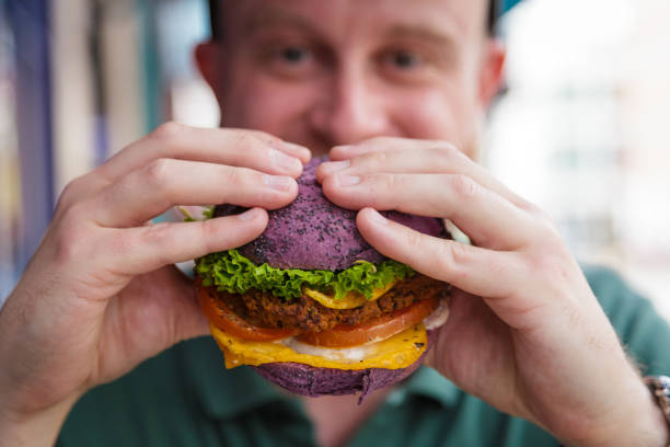 hombre comiendo hamburguesa vegana en bollo de colores - hamburguesa vegetariana fotografías e imágenes de stock