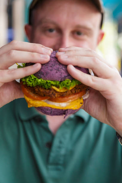 istock Man eating vegan burger in colorful bun 1323358922