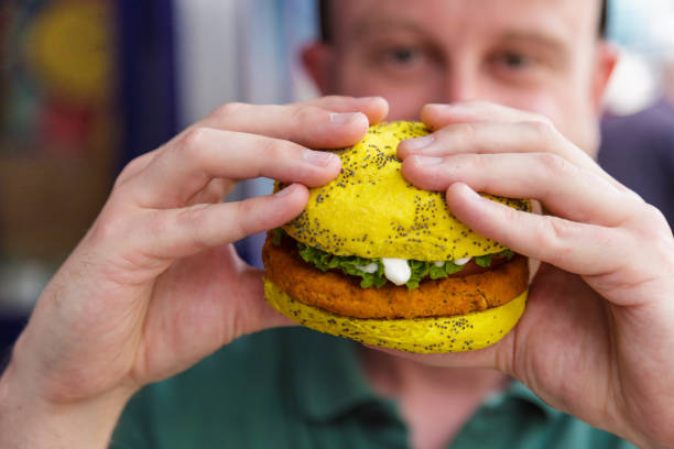 istock Man eating vegan burger in colorful bun 1323358929