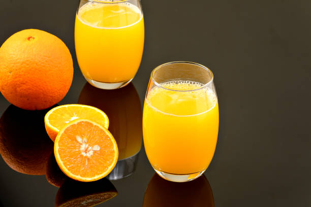istock two glasses with orange juice on a reflective dark surface 1323359971