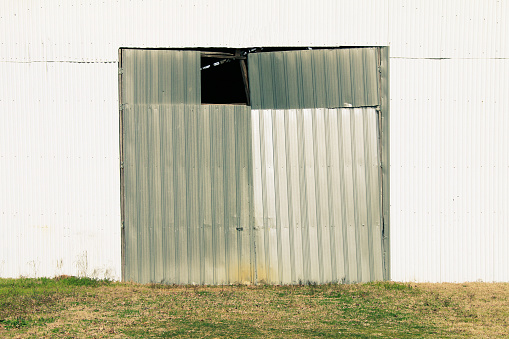 A white steel corrugated metal siding farm warehouse building facade with weathered aged broken sliding doors.